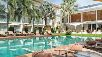 A poolside area with lounge chairs, umbrellas, and a view of a modern building with large windows and palm trees.
