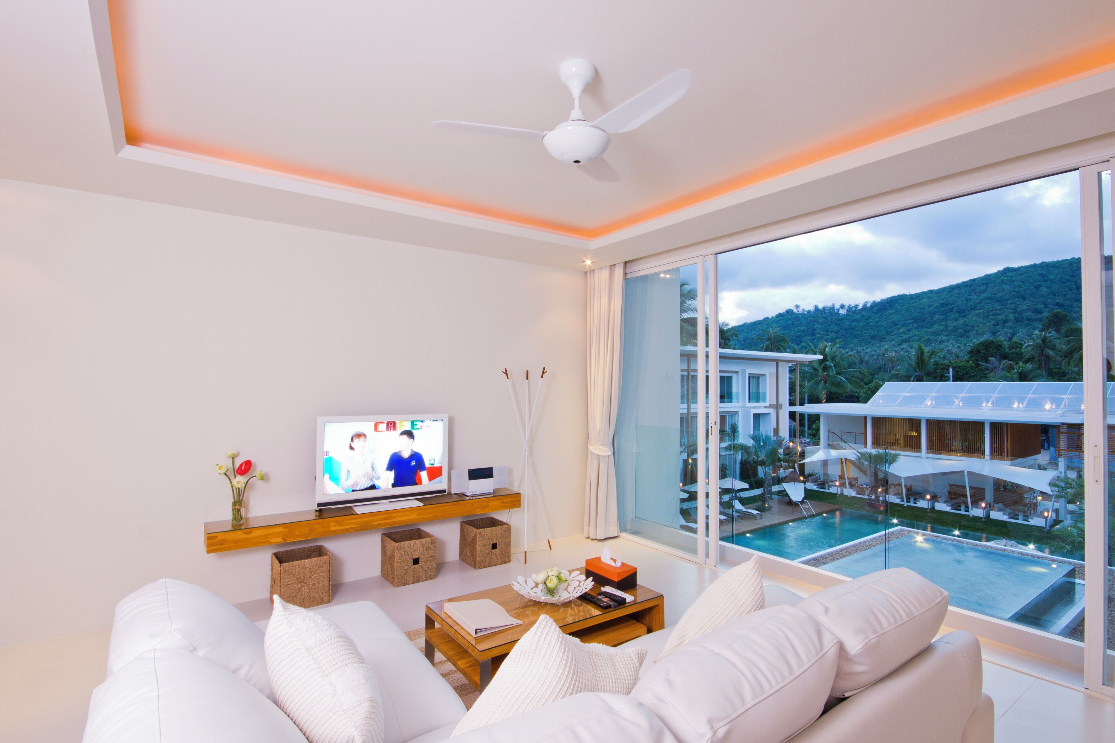 Una sala de estar moderna con un ventanal grande, un ventilador de techo y un televisor de pantalla plana.