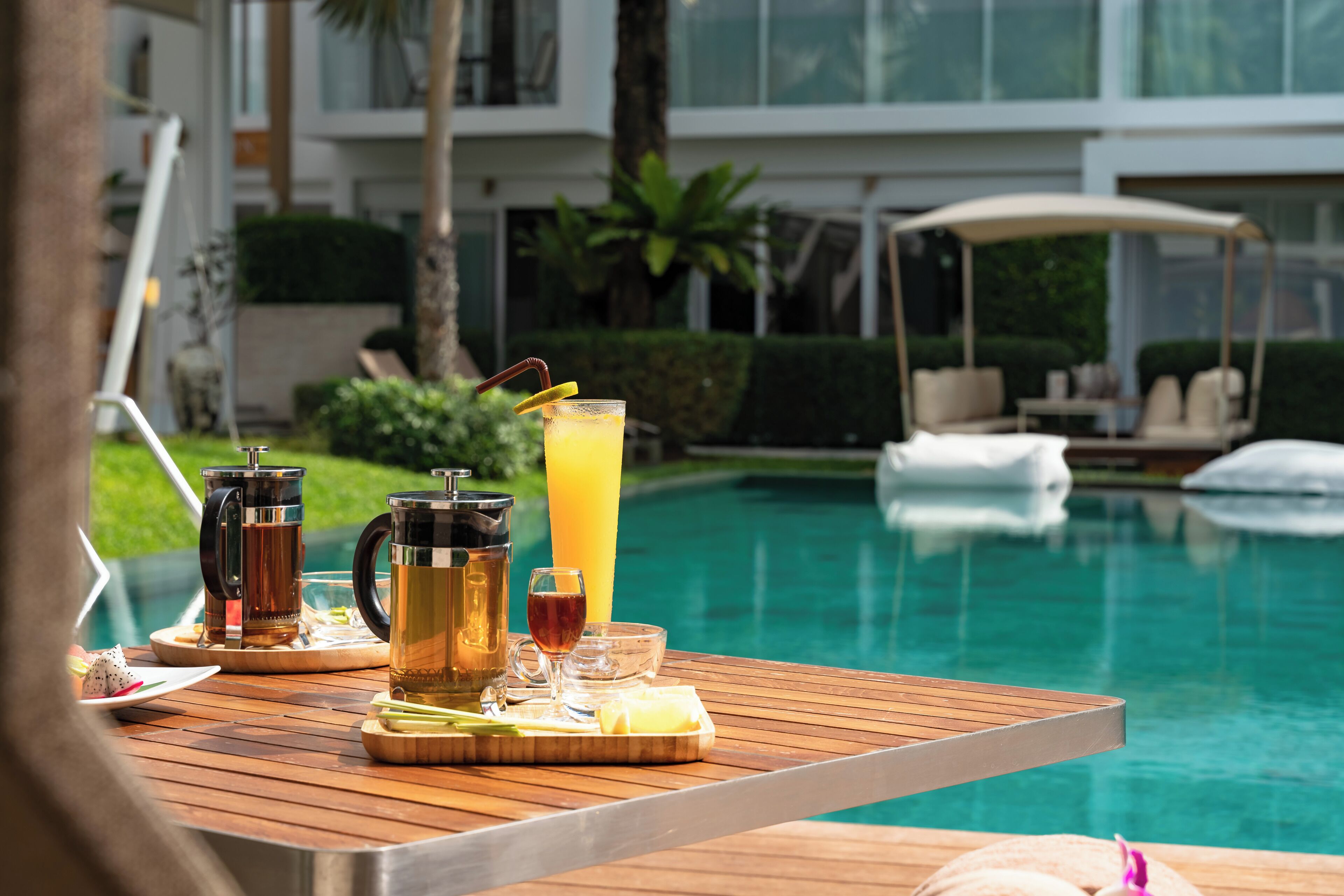 A wooden table with a beverage tray, a pitcher, and glasses by a poolside.