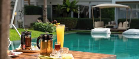 A wooden table with a beverage tray, a pitcher, and glasses by a poolside.