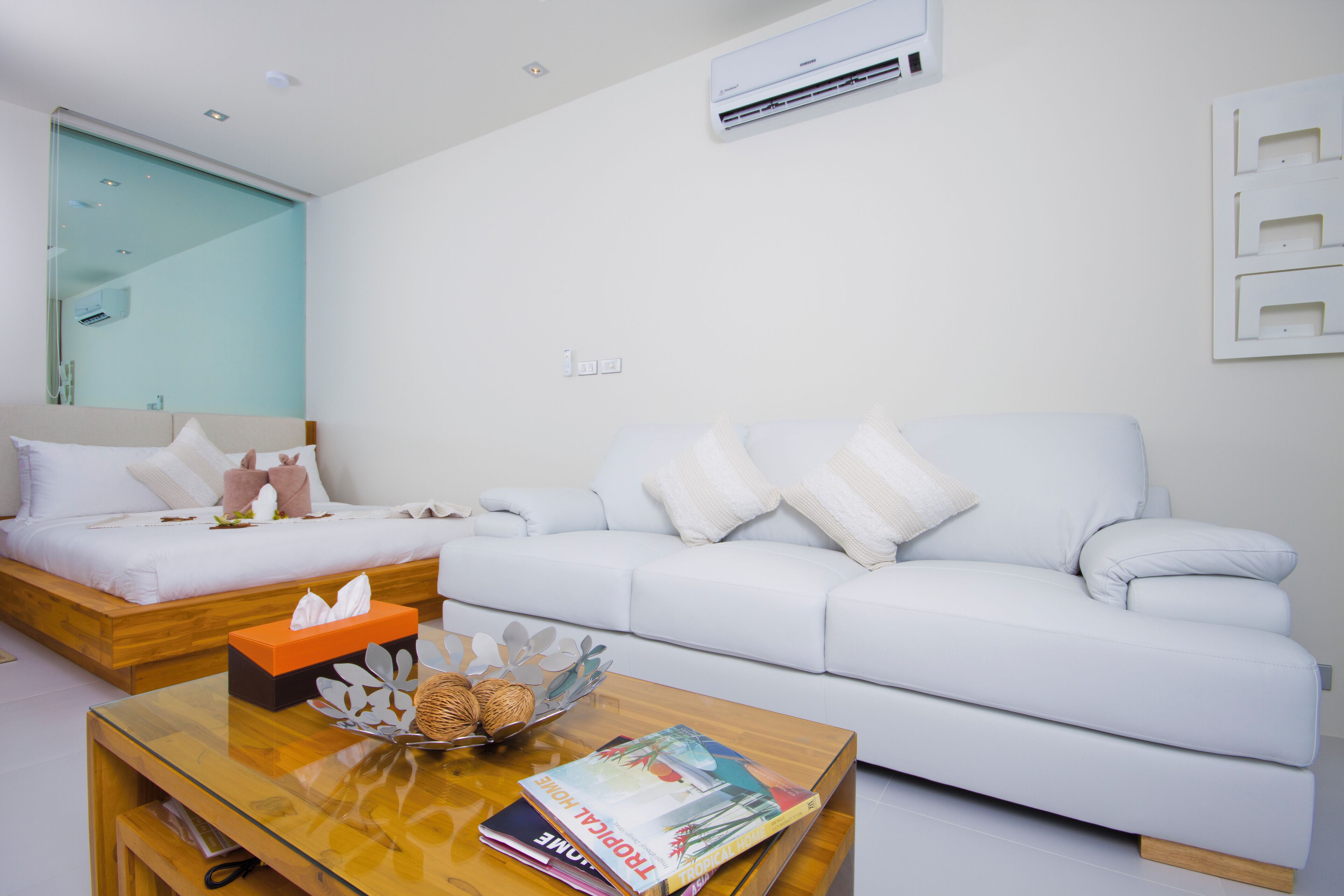 Een moderne hotelkamer met een bed, een witte bank, een houten salontafel met tijdschriften en een wandairconditioning.