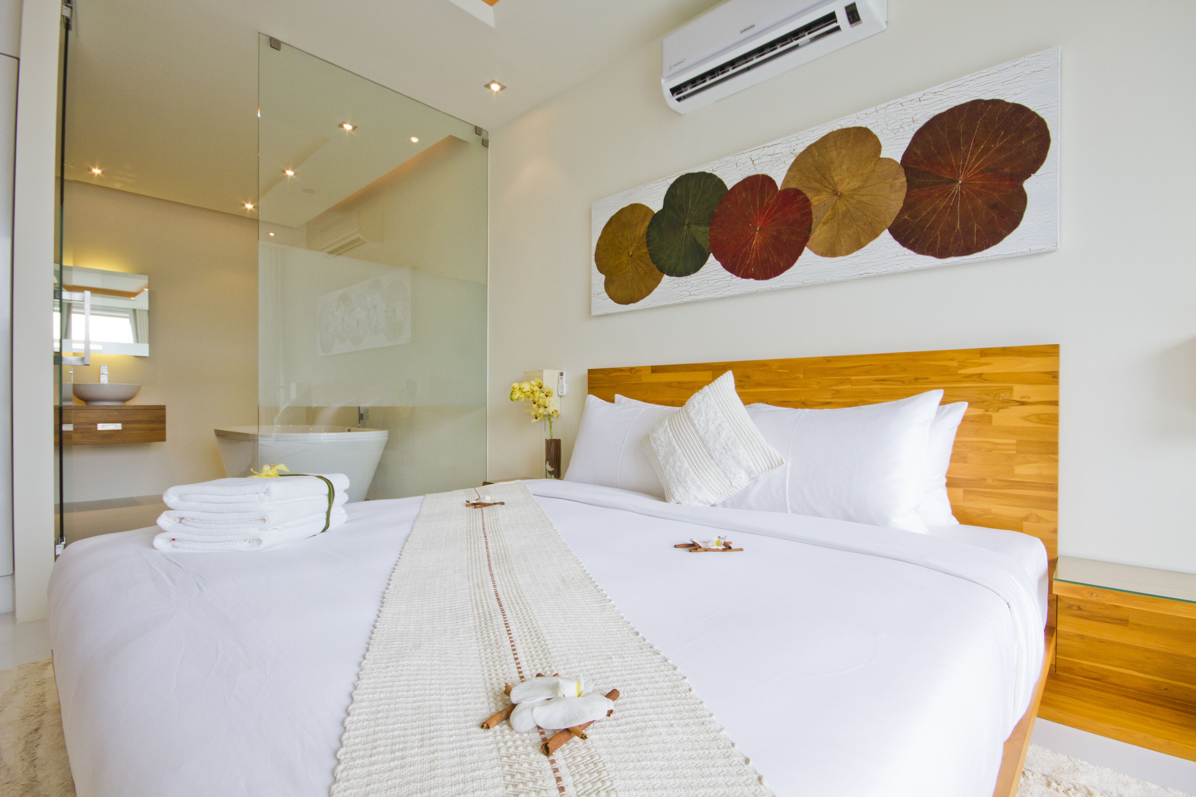 Una habitación de hotel con una cama grande, cabecera de madera, aire acondicionado de pared y una pieza de arte decorativa con hojas.