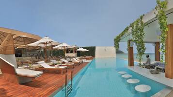 Un espace piscine aménagé sur le toit, avec des chaises longues, des parasols et un bar.