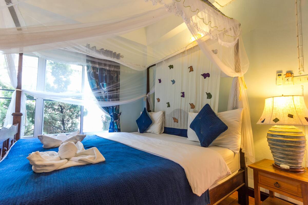 A bed with a canopy, a bedside lamp, and a window with curtains.