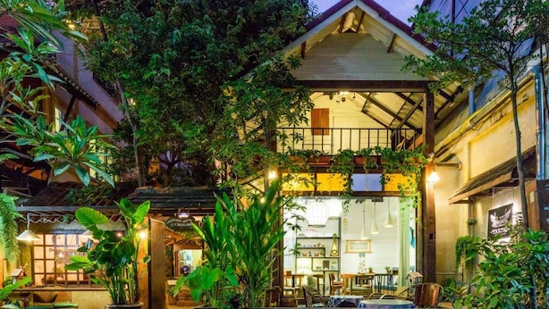 Un bâtiment à deux étages doté d’un balcon, entouré d’une végétation luxuriante et agrémenté de plantes en pot.