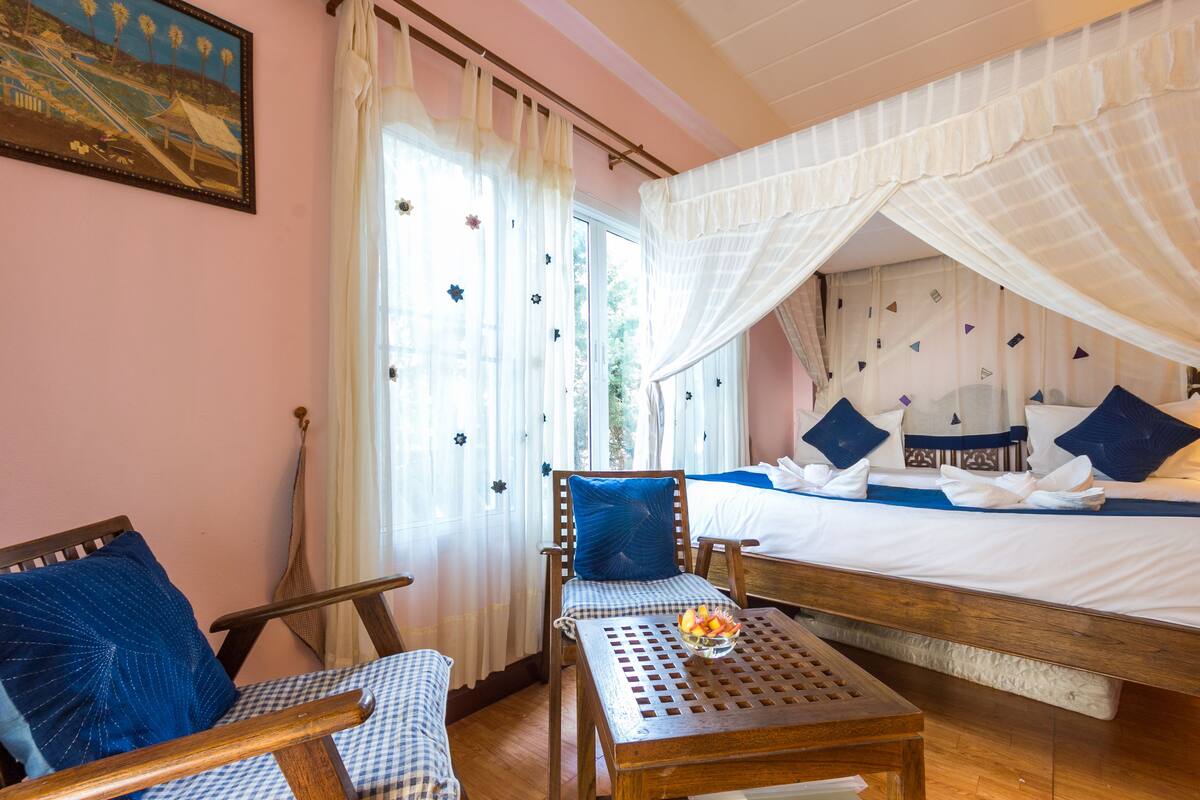A bedroom with a bed, a chair, a table, and a window with curtains.