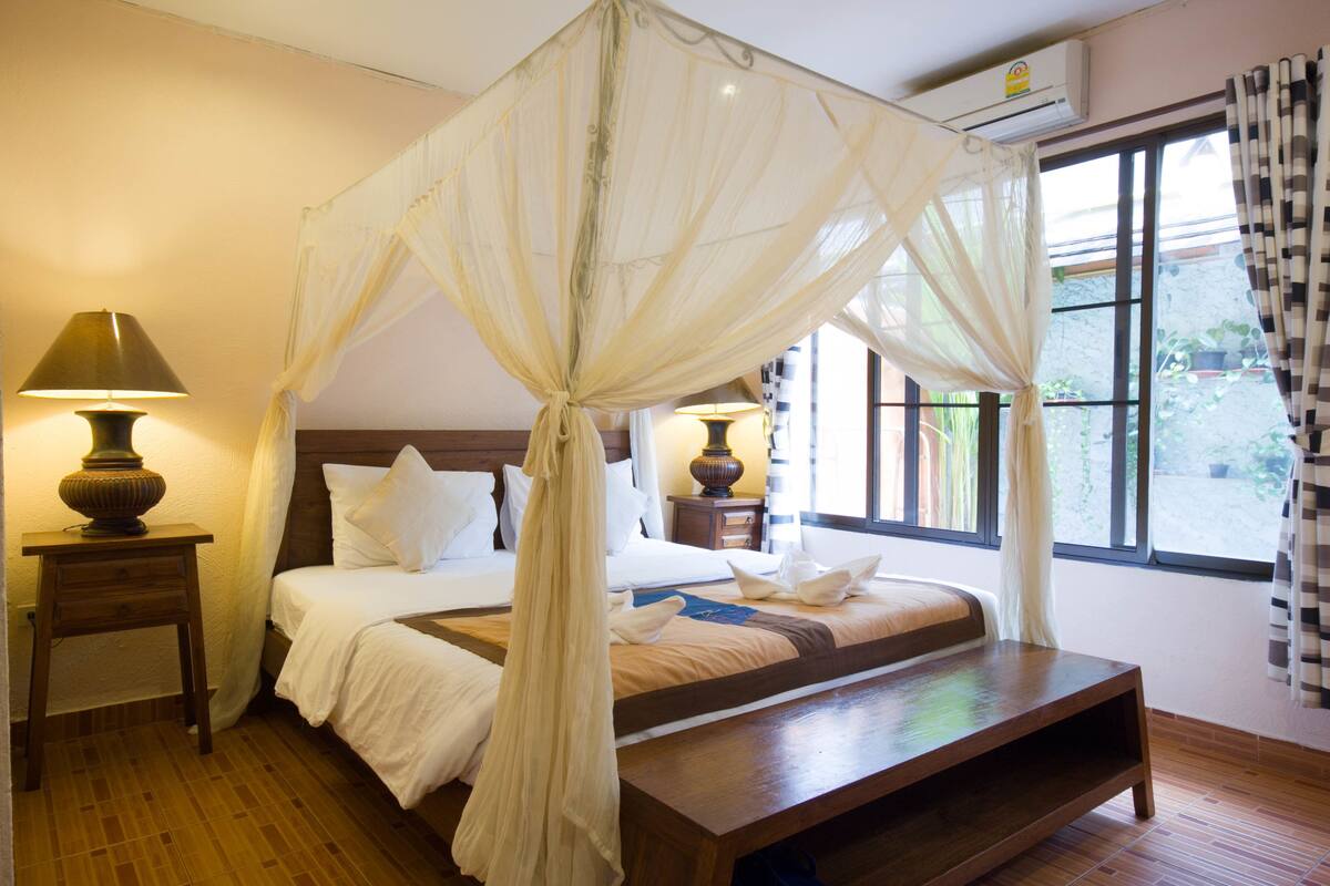 A bedroom with a canopy bed, bedside tables, a lamp, and a view of the outdoors through large windows.