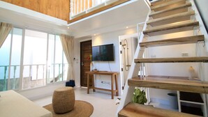 Un vaste espace de vie agrémenté d’un escalier en bois, d’un téléviseur à écran plat et de grandes fenêtres offrant une vue sur l’extérieur.
