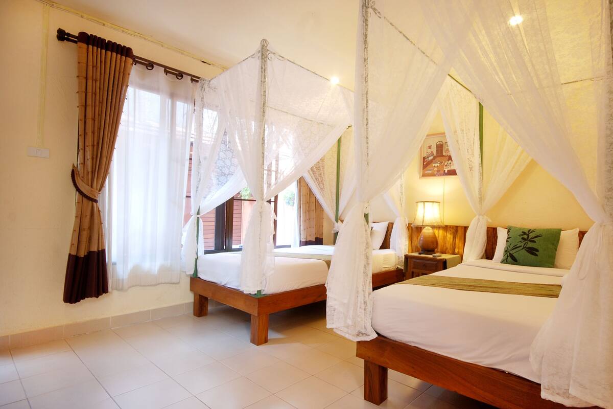 A room with two beds, each with a canopy, a bedside table with a lamp, and a window with curtains.