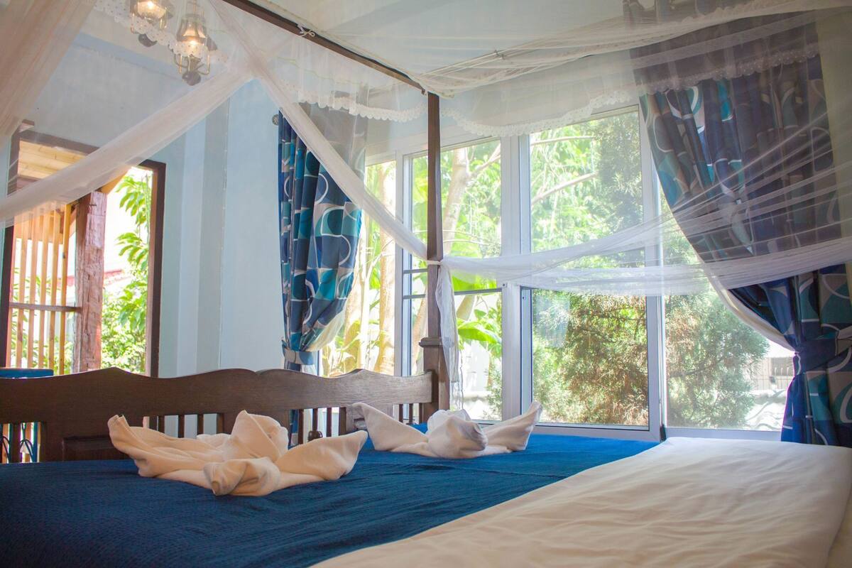 A bedroom with a bed, a canopy, and large windows with curtains.