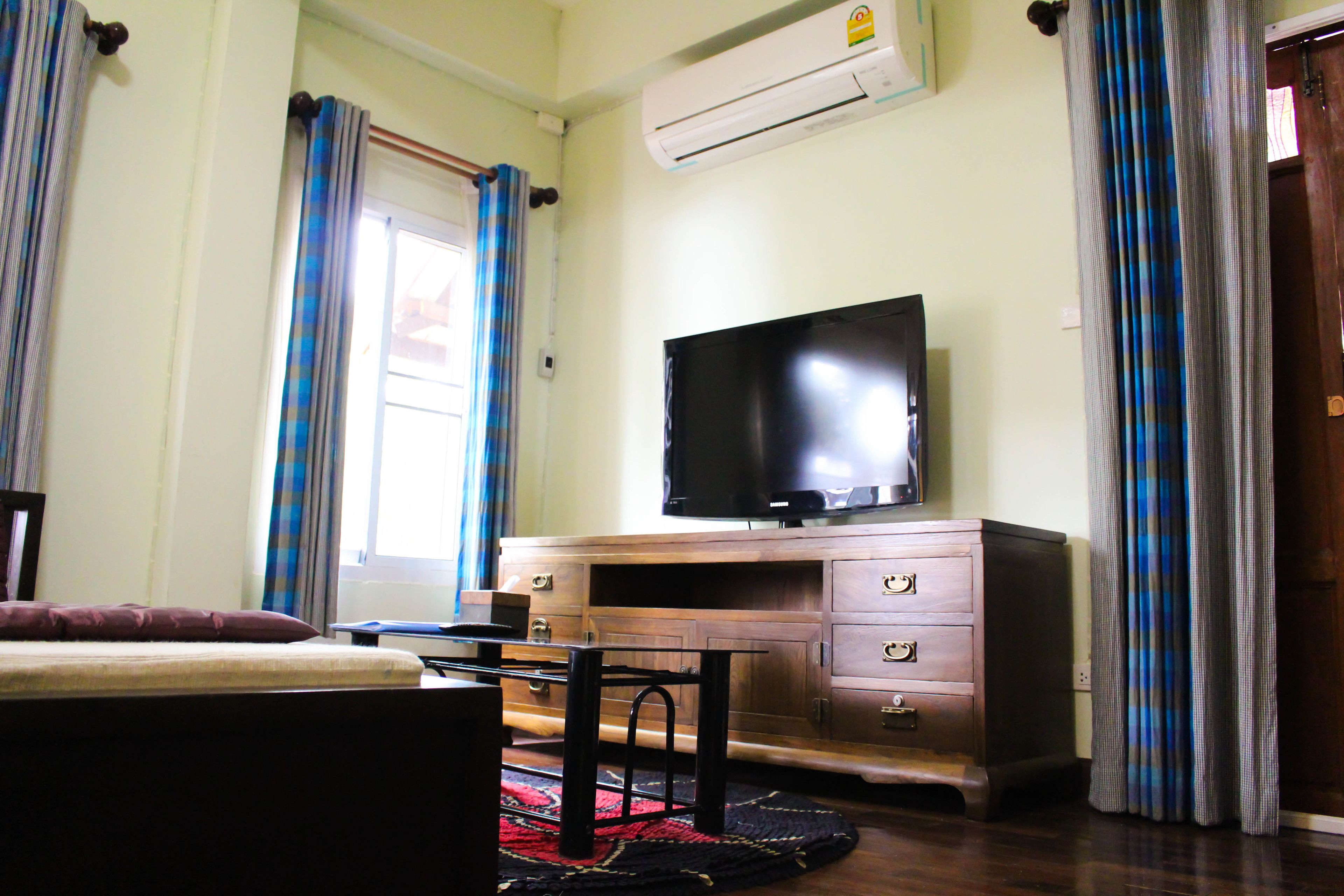A bedroom with a bed, a TV on a wooden cabinet, an air conditioner, and curtains.