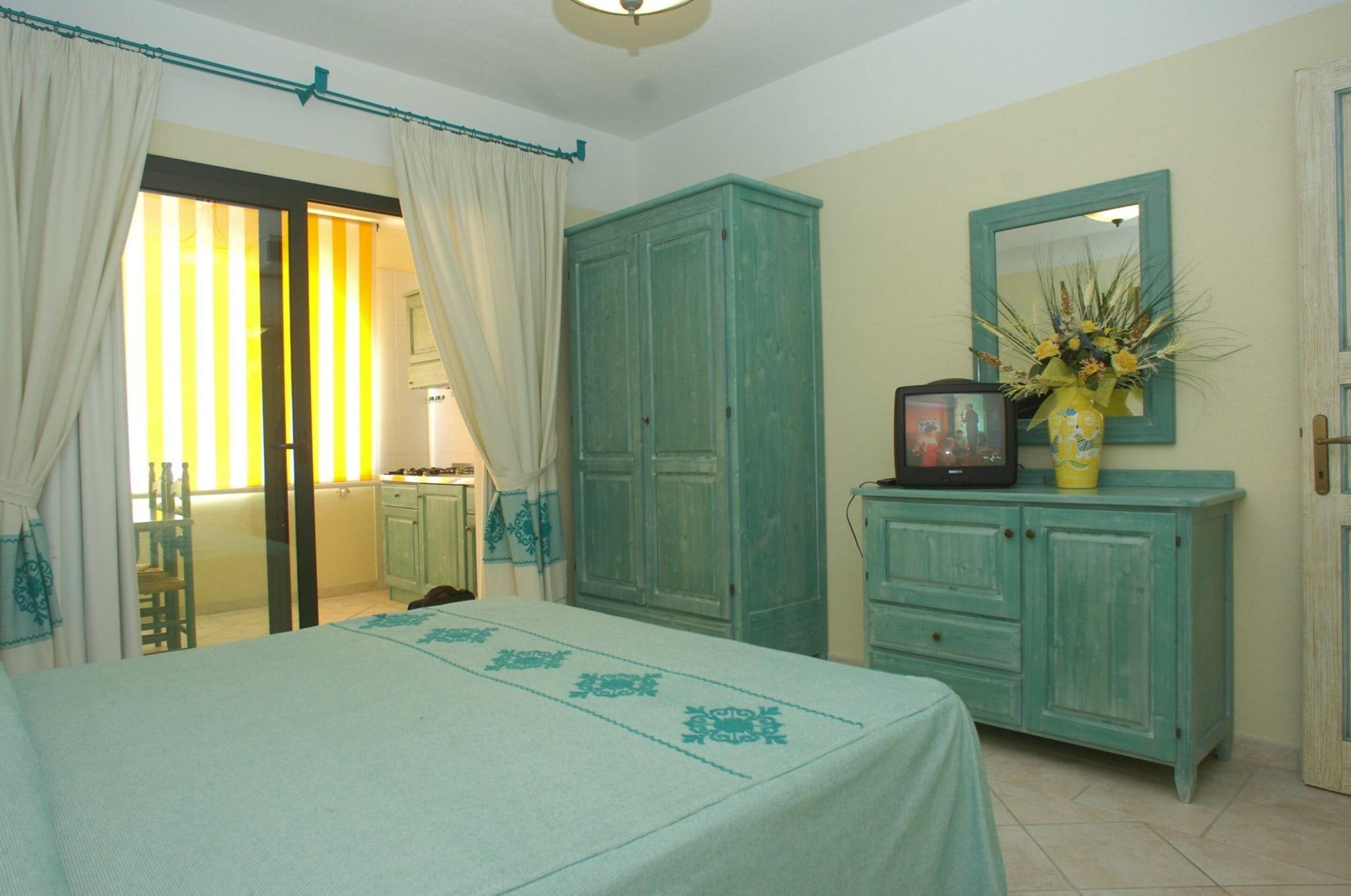 A bedroom with a bed, a wardrobe, a television, and a mirror.