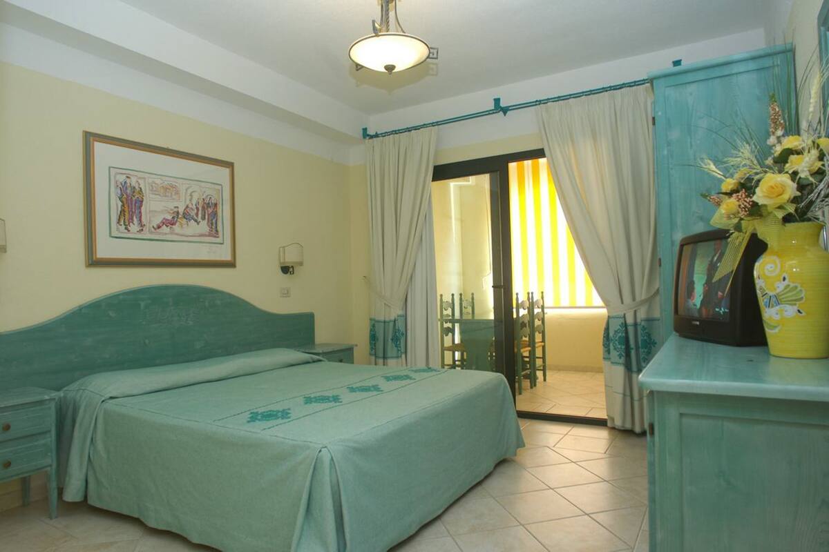 A bedroom with a bed, a desk, a chair, a television, and a window with curtains.