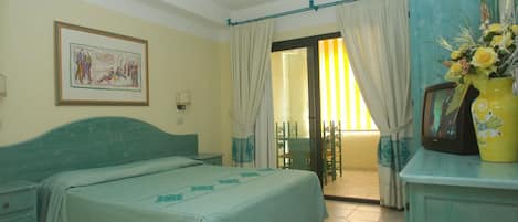Un dormitorio con cama, escritorio, silla, televisor y ventana con cortinas.