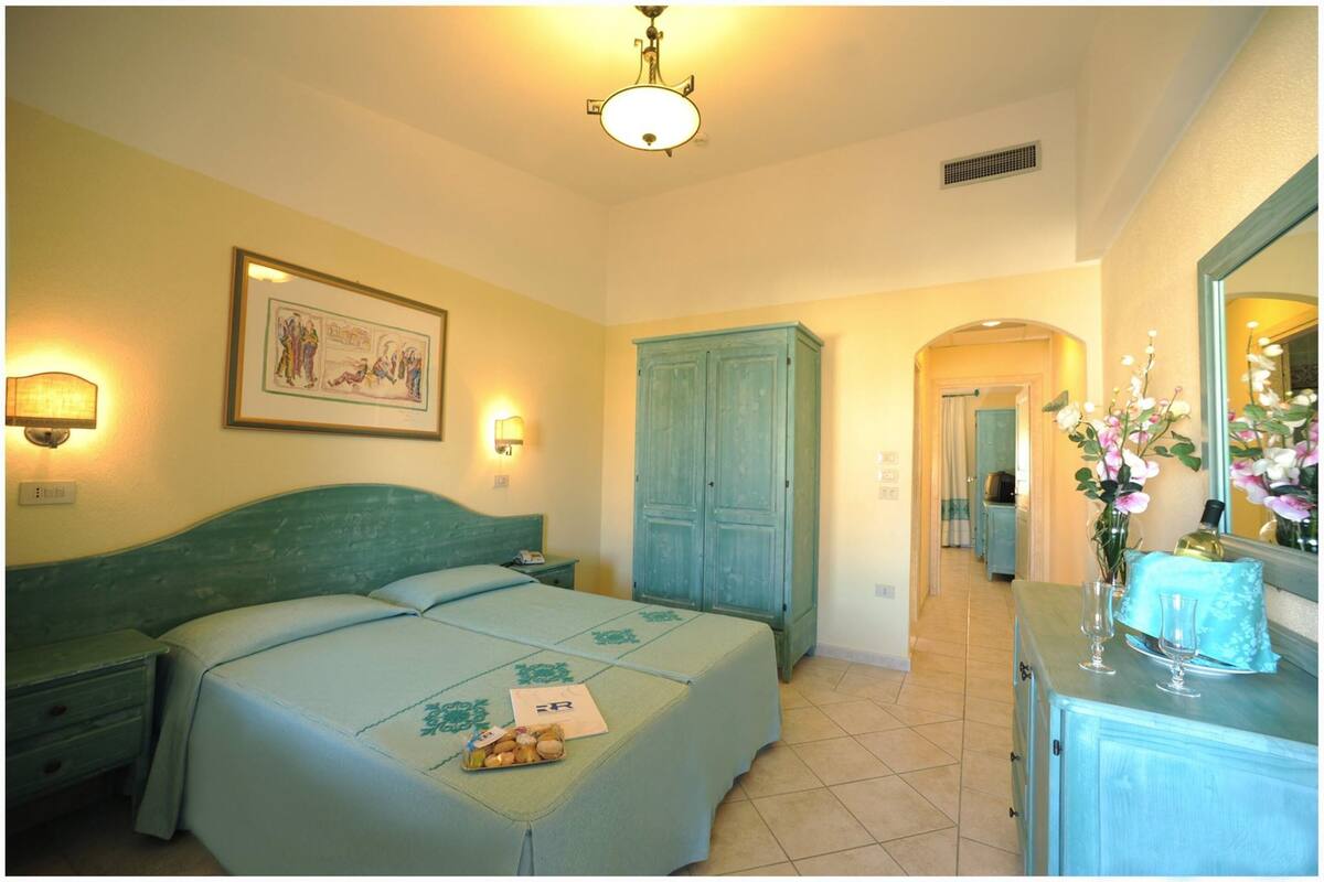 A bedroom with a bed, a dresser, a mirror, and a wall-mounted light fixture.