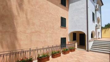 Un bâtiment à l’extérieur beige, avec une partie supérieure blanche et une cour dallée agrémentée de jardinières.