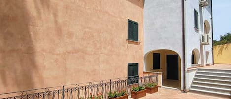 A building with a beige exterior, white upper section, and a tiled courtyard with planters.