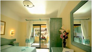 Habitación de hotel con cama, escritorio, espejo, un jarrón de flores y un balcón con vistas.