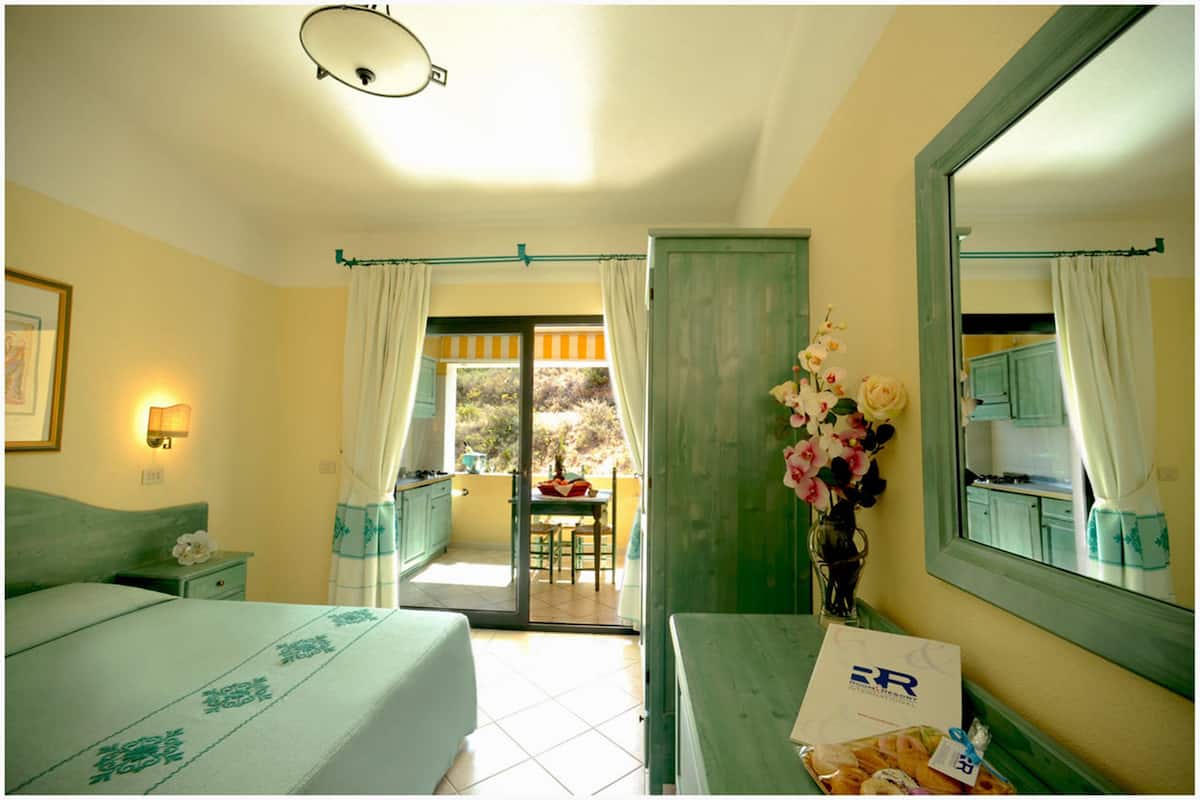A hotel room with a bed, a desk, a mirror, a vase of flowers, and a balcony with a view.