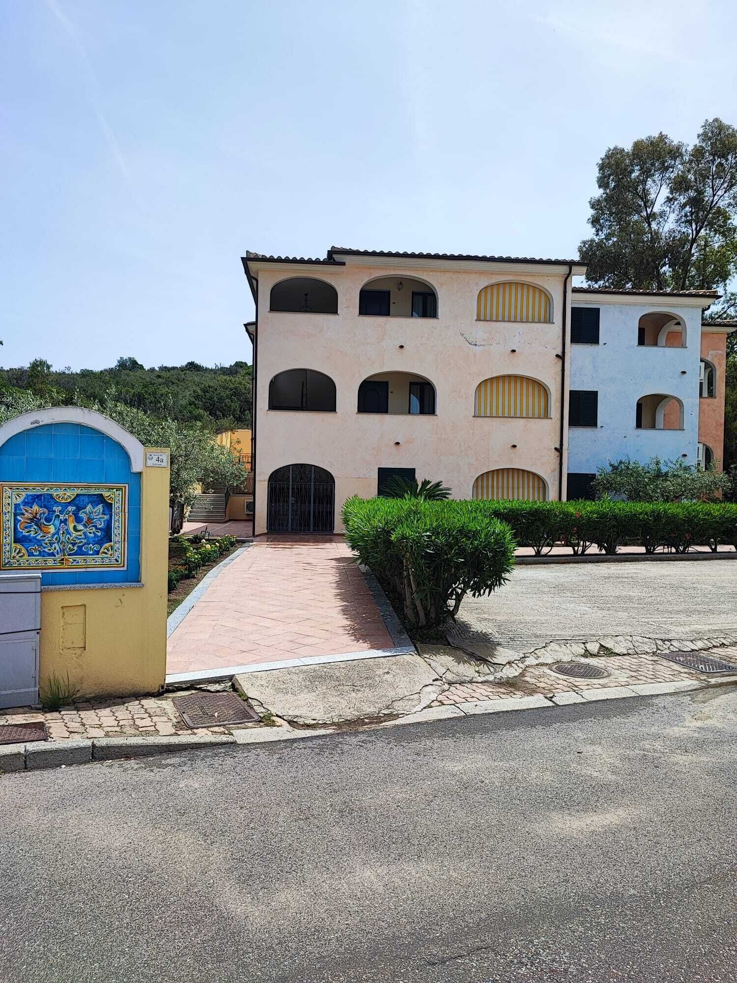 A building with a tiled entrance, a blue door with a decorative tile, and a paved pathway leading to the entrance.