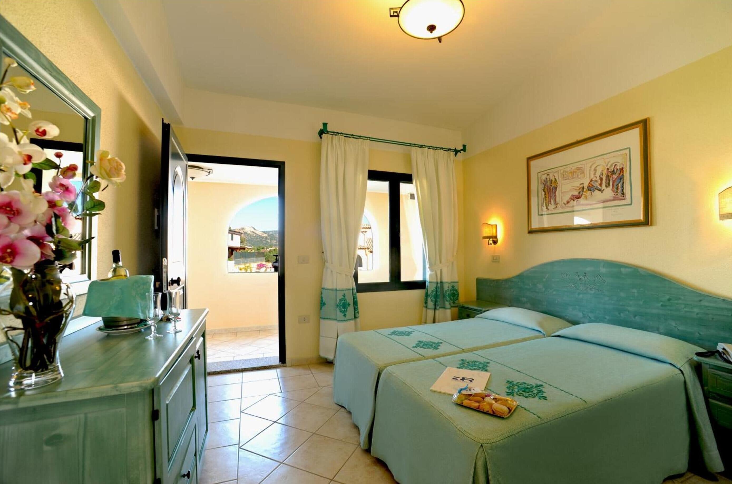 A hotel room with two beds, a dresser, a vase of flowers, and a painting on the wall.