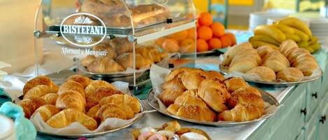 A buffet with various baked goods, including croissants and pastries, and a display case labeled "BISTEFANI".