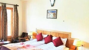 A hotel room with a bed, two bedside tables, a nightstand, a window with curtains, and a wall-mounted picture. - TIH Hotel Kidar, Leh (Leh)