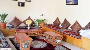 A living room with a sofa set, a coffee table, and a small table with a vase of flowers. There are framed pictures on the wall. - TIH Hotel Kidar, Leh (Leh)