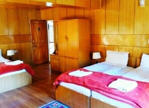 A hotel room with wooden paneling, a bed with a red and white bedspread, a wardrobe, and a nightstand with a lamp.