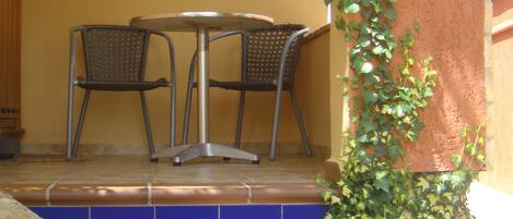 A patio with a table and chairs, a small plant, and a set of stairs leading up to a door.