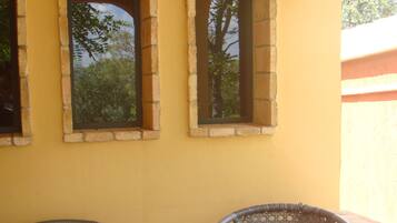 A patio with a round table and two wicker chairs, set against a yellow wall with three arched windows.
