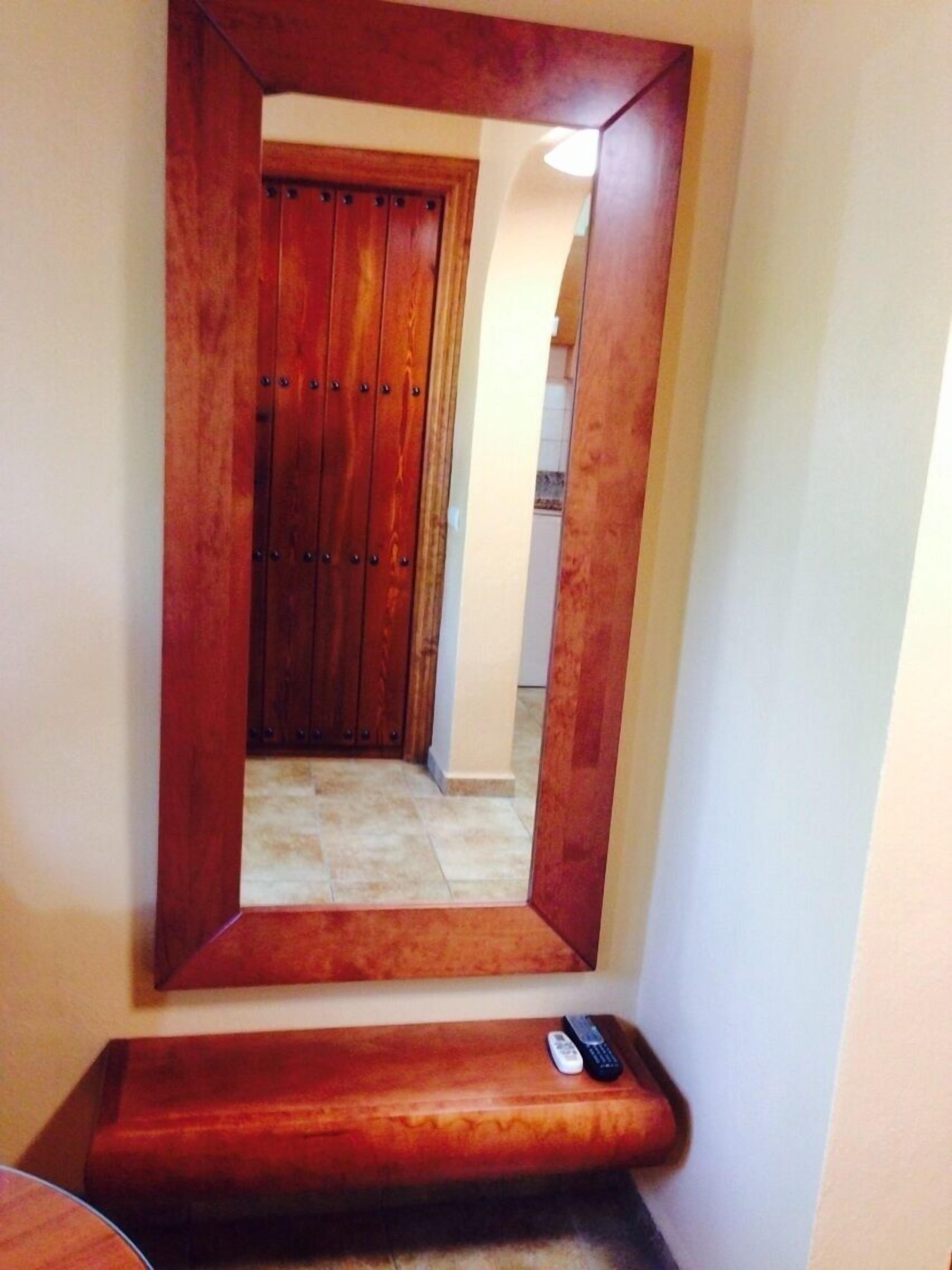 Una porta di legno con uno specchio che riflette un corridoio e un telecomando su una panca di legno.