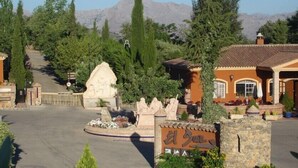 Ein Hotel Eingang mit einem Steinschild, einem angelegten Garten und einem Berg im Hintergrund.