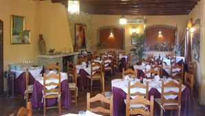 Ein Restaurant mit Holztischen und -stühlen, einem Steinkamin und Wandleuchten.