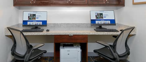 Un espacio de trabajo con dos computadoras de escritorio, sillas de oficina e impresora sobre una encimera de granito.
