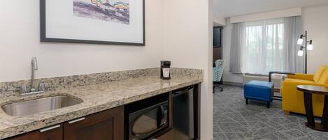 A modern kitchen with granite countertops, a built-in microwave, and a dishwasher. There is a framed picture on the wall and a window with curtains.