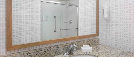 A bathroom with a granite countertop, a white sink, a large mirror, and a shower area.
