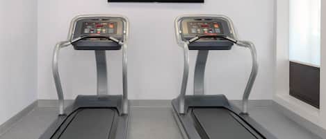 Dos cintas de correr en una sala con un ventanal grande y un televisor de pantalla plana montado en la pared.