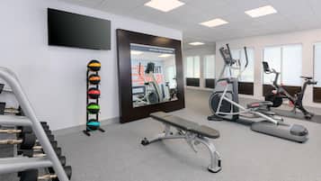 Une salle de sport équipée de matériel d’exercice, d’un banc et d’un téléviseur fixé au mur.