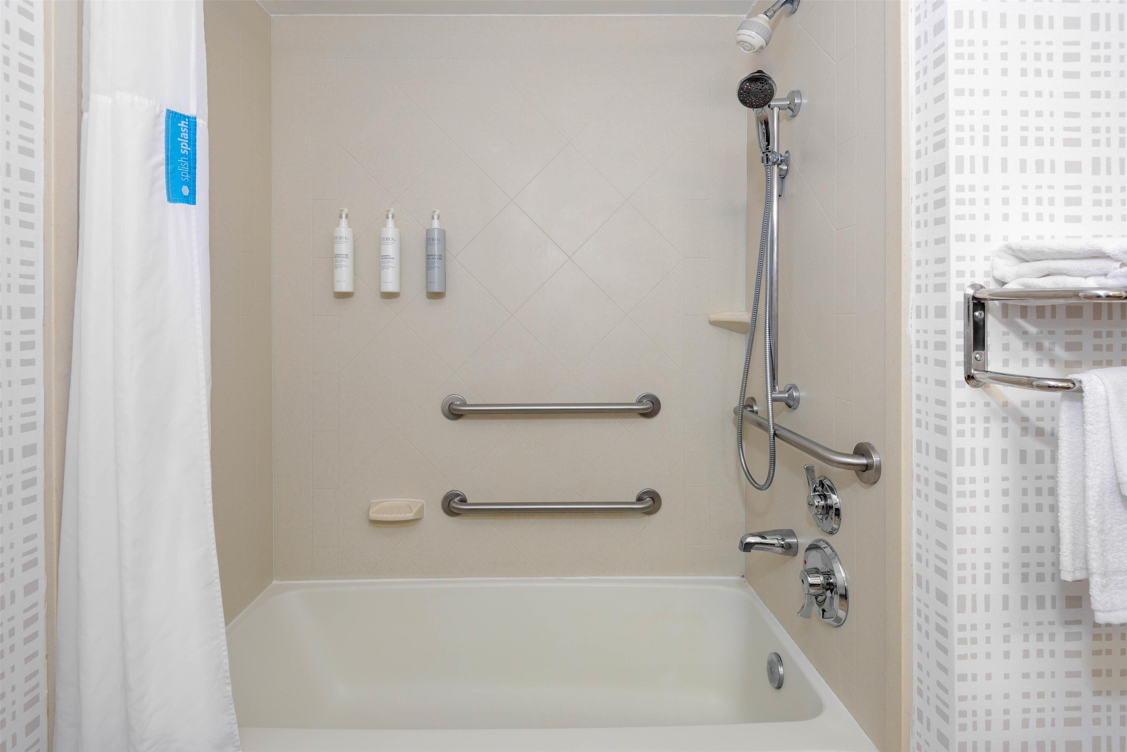Un baño con bañera, barras de apoyo, cabezal de ducha y artículos de aseo.