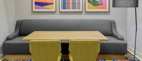 A room with a gray sofa, a wooden table, two yellow chairs, a colorful patterned rug, and three framed artworks on the wall.