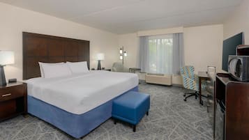 A hotel room with a large bed, a desk with a chair, a microwave, and a window with curtains.