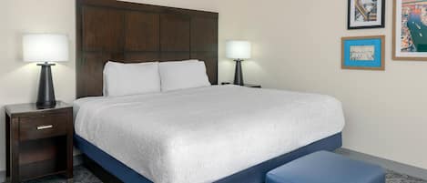 Una habitación de hotel con una cama grande, dos mesitas de noche con lámparas, un reposapiés azul y tres cuadros en la pared.