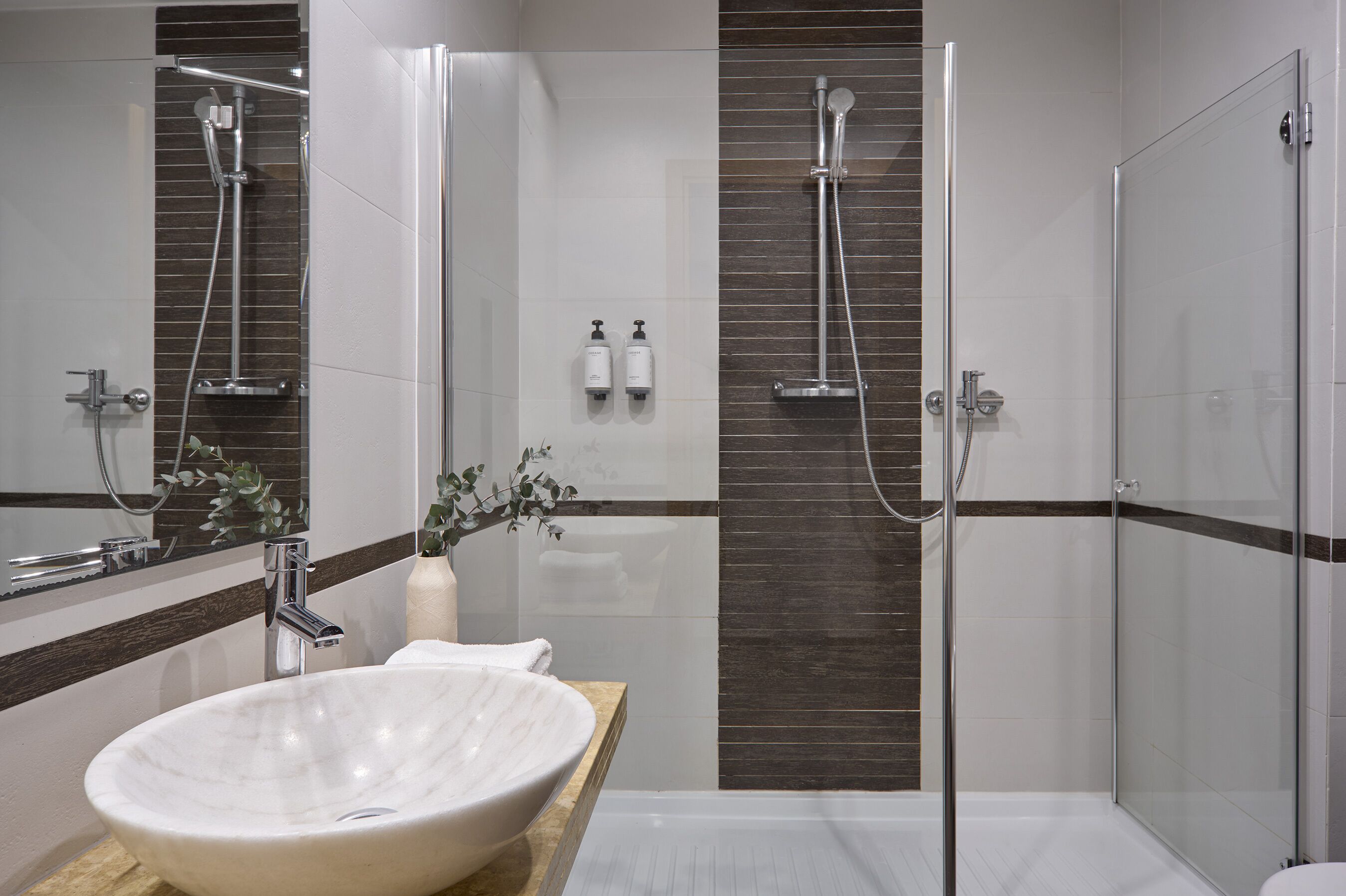 A modern bathroom with a large white sink, a glass-enclosed shower, and a wooden vanity.