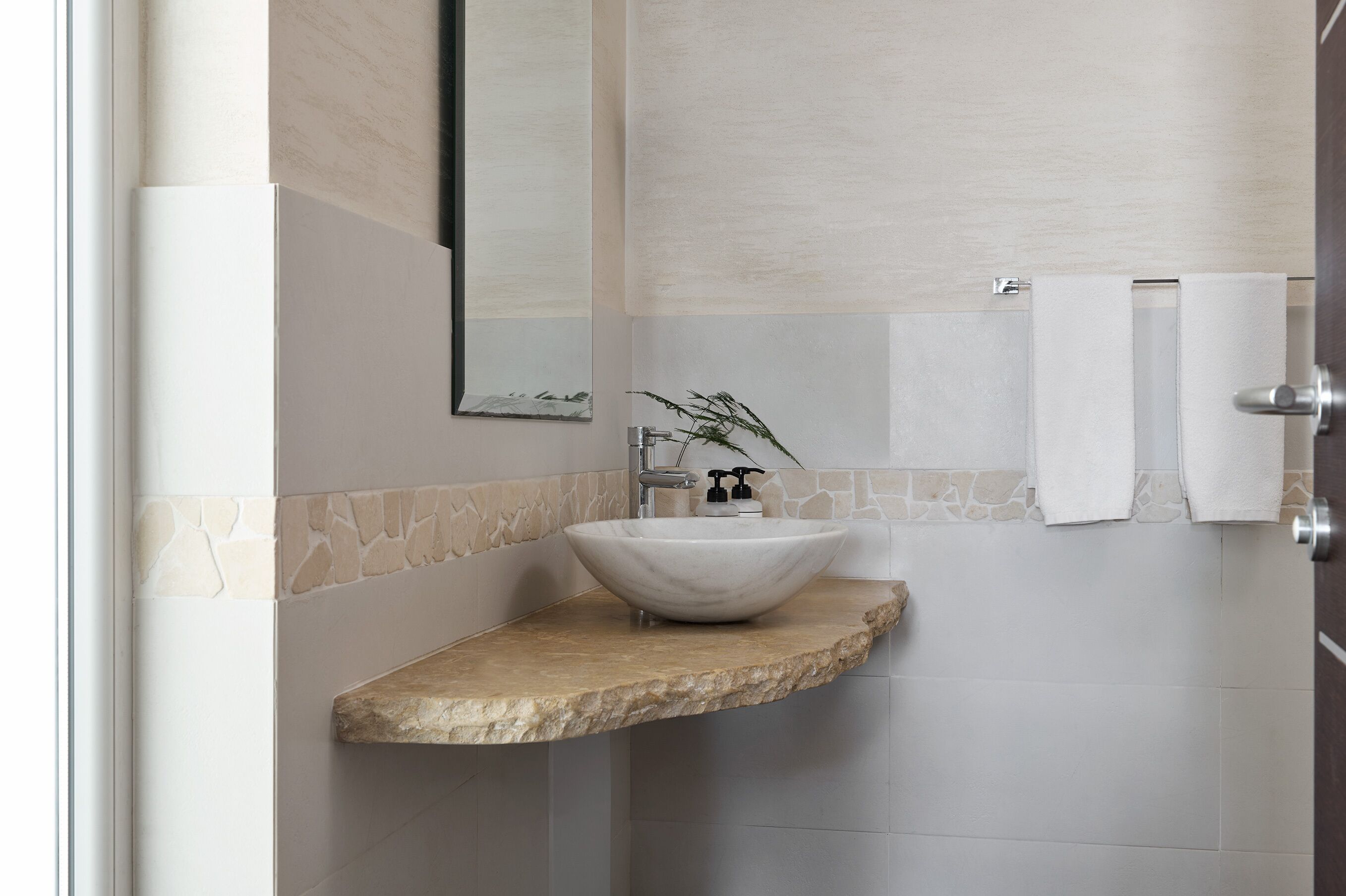 A bathroom with a stone countertop, a white sink, a mirror, and a towel rack.