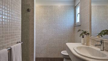 A bathroom with a tiled shower, a sink, and a toilet.