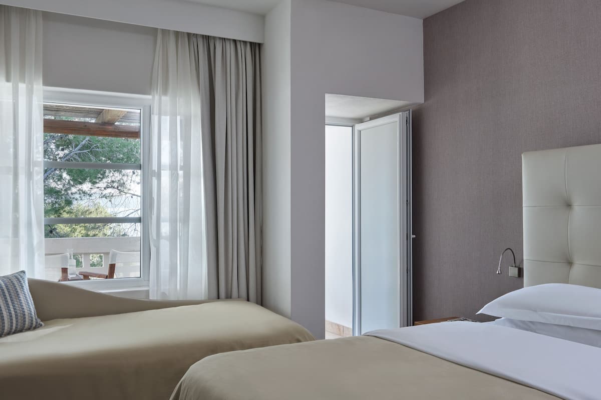 A hotel room with two beds, a large window with curtains, a wardrobe, and a bathroom with a shower.