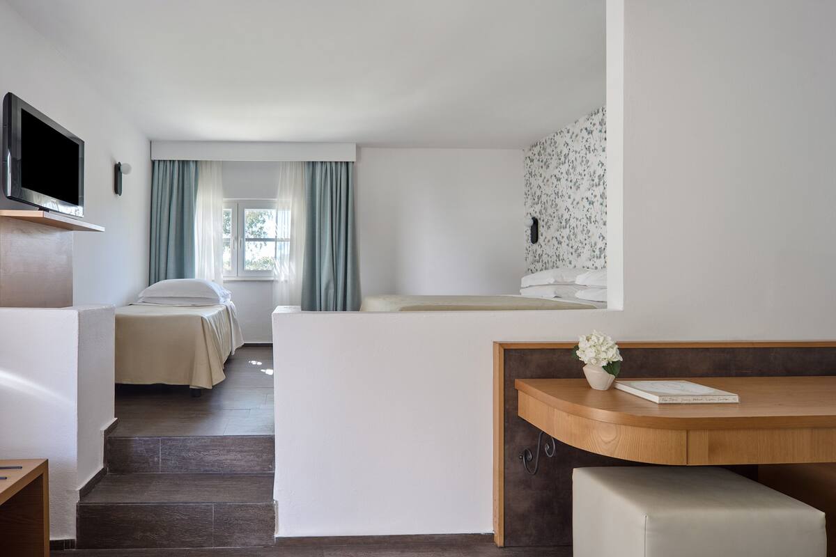 A hotel room with a bed, a desk, a TV, and a window with curtains.