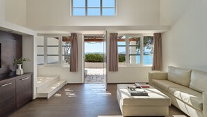 Una sala de estar moderna con sofá, mesa de centro, televisor y ventanas amplias con cortinas.