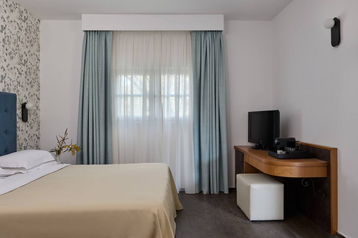 A hotel room with a bed, a desk with a television, and a window with curtains.